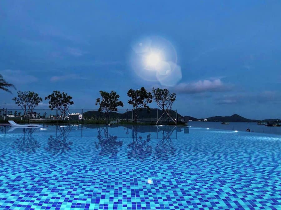 Una piscina con suelo de baldosas, rodeada de árboles y vistas al mar.