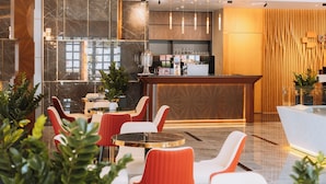 Un moderno vestíbulo de hotel con mostrador de recepción, zona de estar con sillas rojas y blancas, y área de bar.