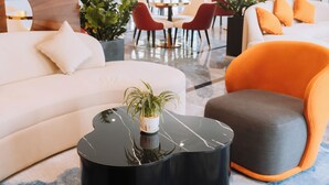 Un área de estar moderna con un sofá blanco, un sillón naranja y una mesa de centro negra con una planta.