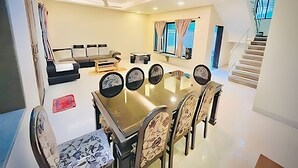 Ein geräumiges Wohnzimmer mit großem Esstisch, bequemen Sitzgelegenheiten, einer Treppe und Blick ins Freie.