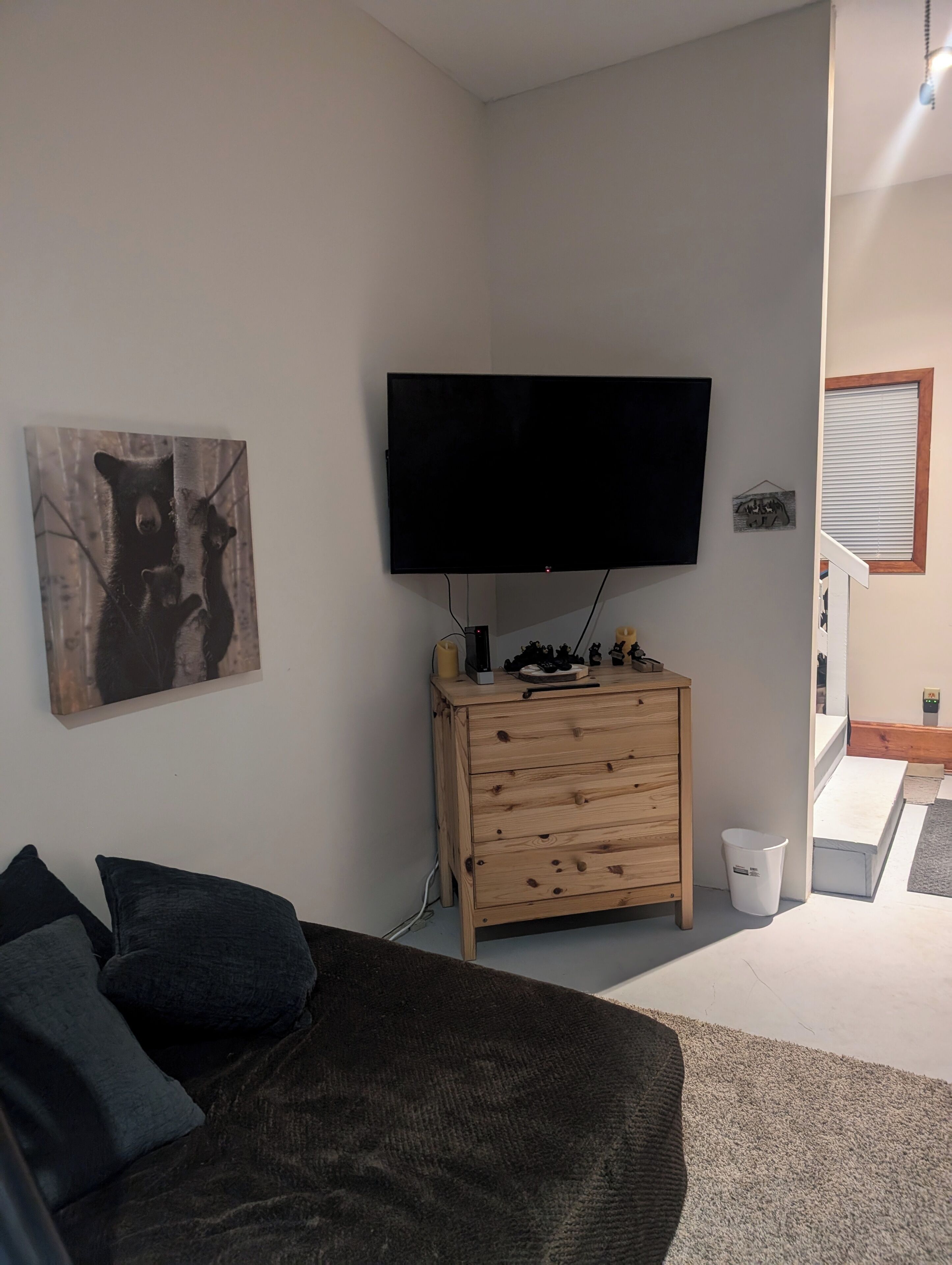 Una sala de estar con un televisor de pantalla plana en la pared, un aparador de madera, un sofá con cojines y un cuadro de osos.
