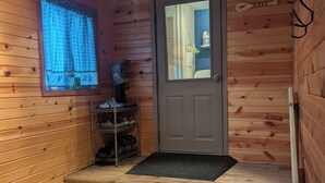 Une cabane en bois avec une porte, une fenêtre avec des rideaux, un porte-chaussures et une petite marche menant à la porte.