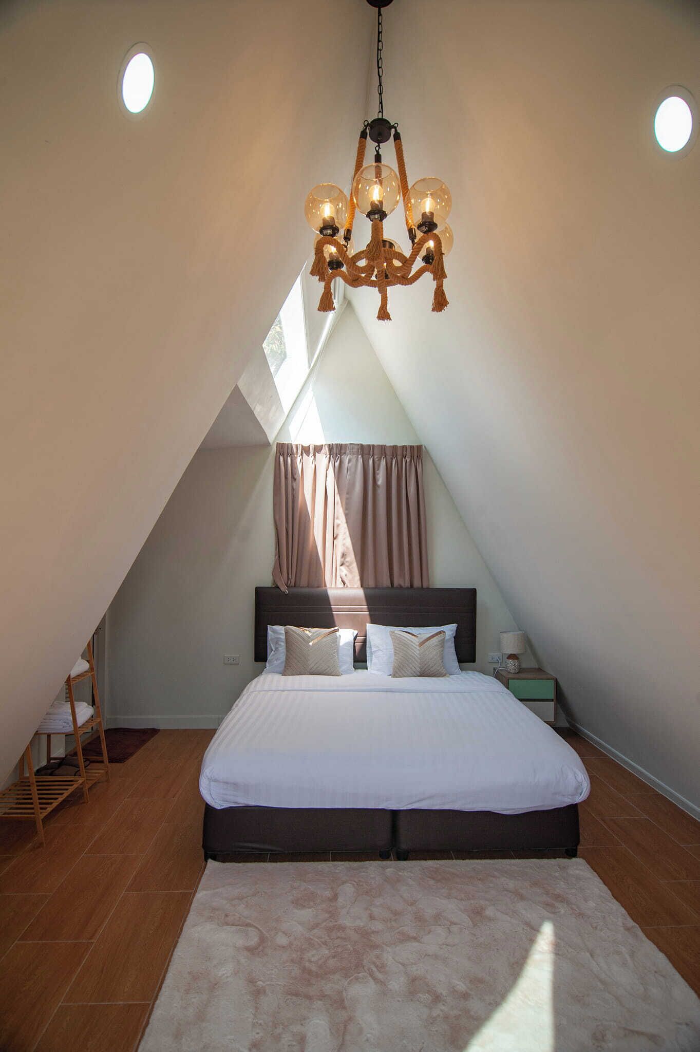 A bedroom with a sloped ceiling, a bed with a headboard, a chandelier, and a nightstand with a lamp.