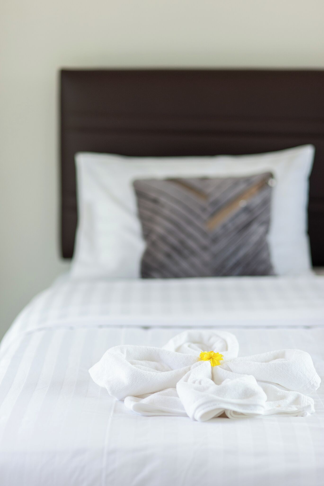Una cama bien hecha con ropa blanca y una toalla doblada con una flor amarilla.