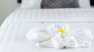 Una cama bien hecha con ropa blanca y una toalla doblada con una flor amarilla.