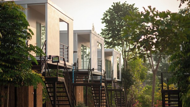 Une rangée de maisons modernes au style minimaliste, dotées d’escaliers extérieurs menant aux étages supérieurs, et entourées d’une végétation luxuriante et de plantes en pot.