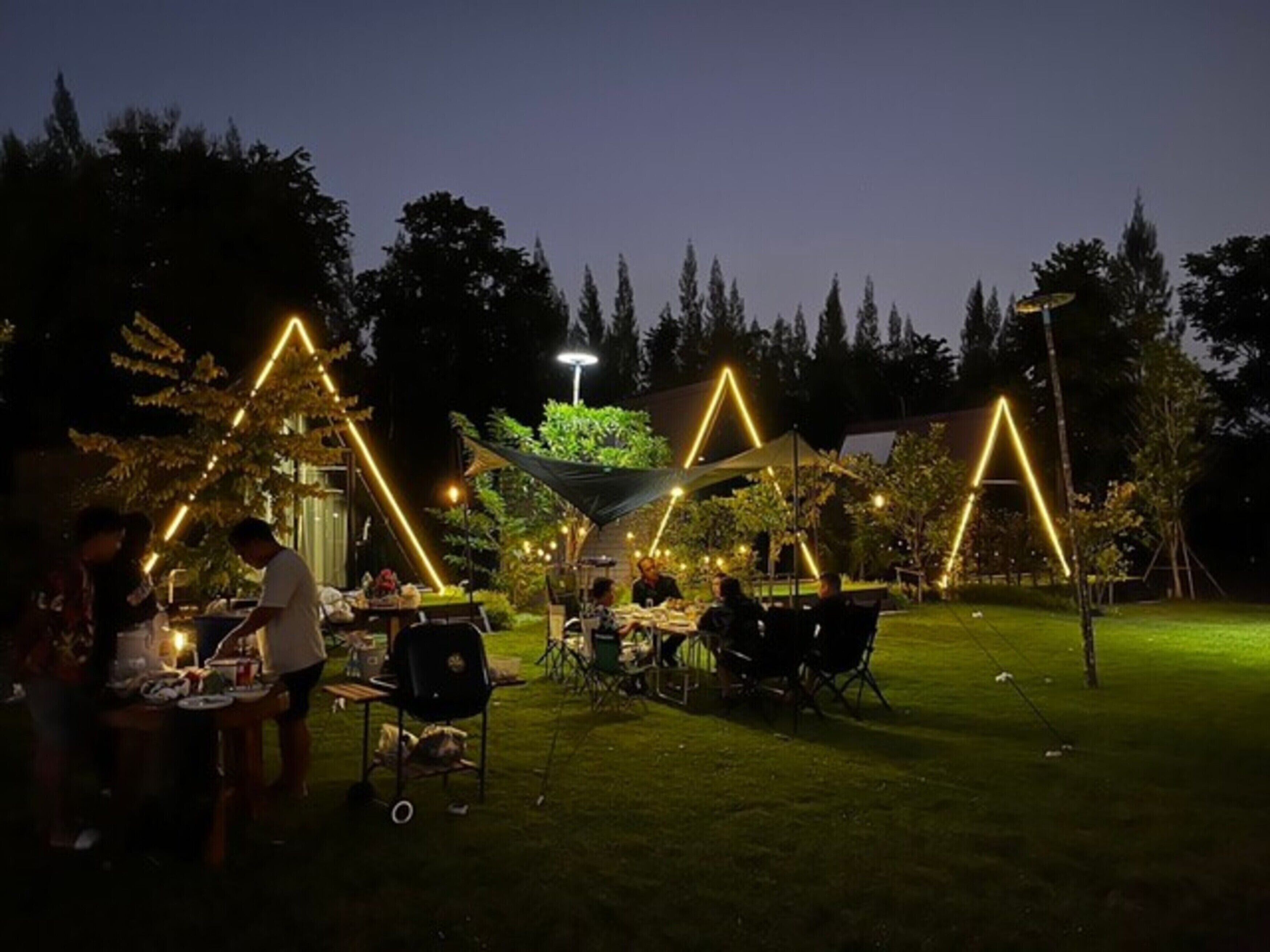 An outdoor dining area with tables and chairs, illuminated by string lights forming triangular patterns.