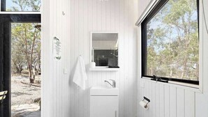 A modern bathroom with a white sink, a mirror above it, and a window providing a view of trees. - Bilby Park Escape 1 by Tiny Away (Black Range)