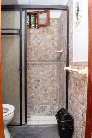 Un baño con zona de ducha, inodoro y cubo de basura.