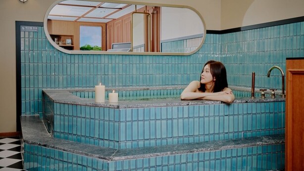 A bathroom with a blue-tiled bathtub, a mirror, and a black and white checkered floor. - Stay Passport Express Spa Dangsan (Seoul)