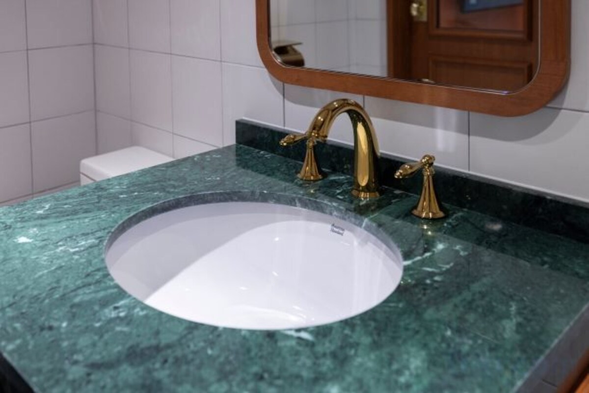 A bathroom with a white sink, green marble countertop, and a gold faucet.