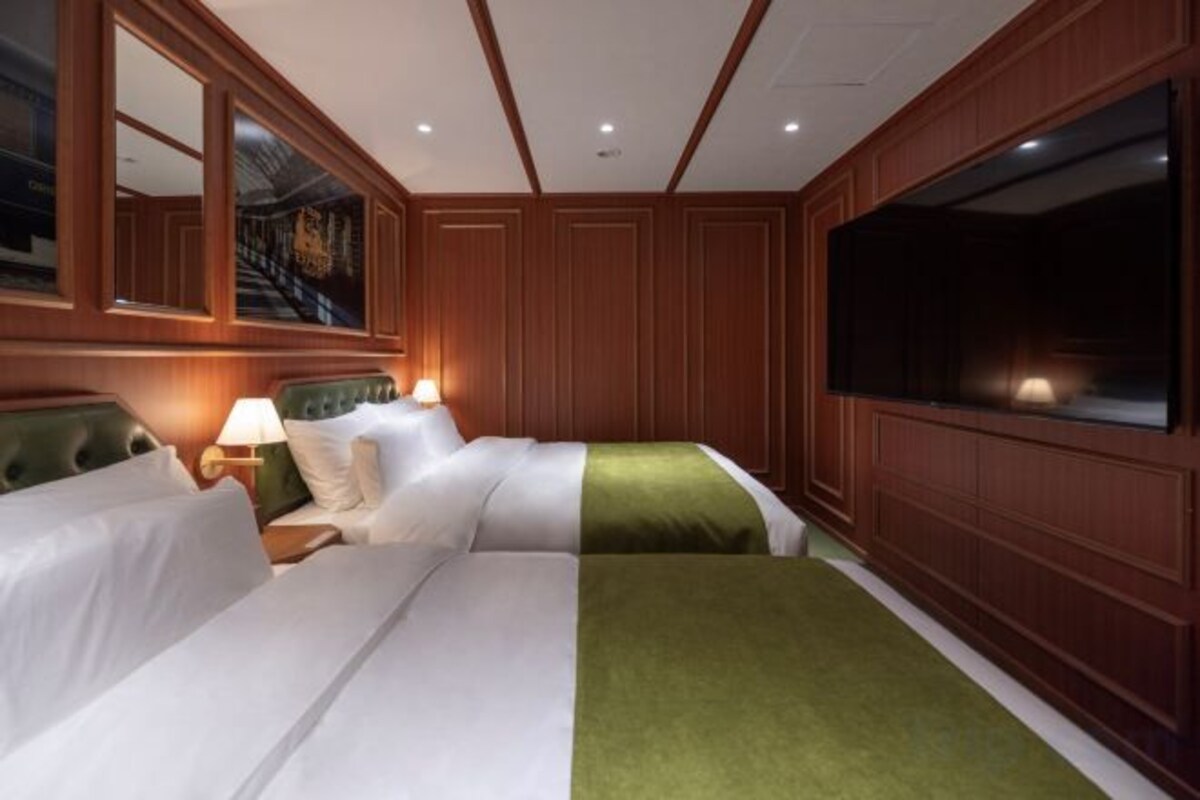 A hotel room with two beds, a large window, and a wall-mounted TV.