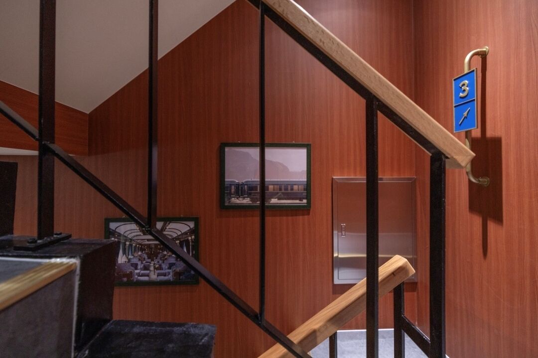 A wooden staircase with a metal handrail, a blue sign with the number 3, and framed pictures on the walls.