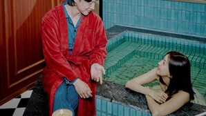 A person in a red robe sitting by a bathtub with a tiled wall and wooden paneling in the background. - Stay Passport Express Spa Dangsan (Seoul)