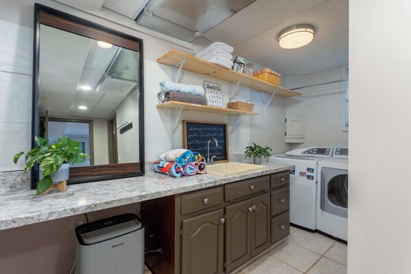 A modern kitchen with a marble countertop, a sink, a washing machine, and a chalkboard with a message. - Lakefront Oasis:Big Back Porch, Private Pool & Hot Tub! All on Lake Chickamauga (Decatur)