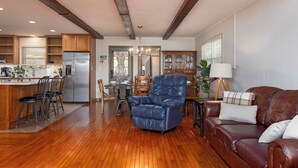 A spacious living area with a wooden floor, a blue leather armchair, a brown leather sofa, and a dining area with a chandelier. - Lakefront Oasis:Big Back Porch, Private Pool & Hot Tub! All on Lake Chickamauga  (Decatur)