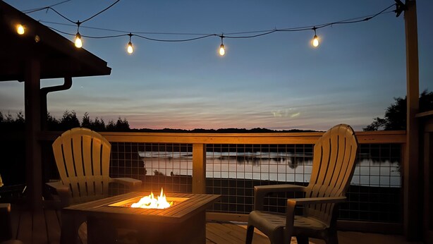 A deck with two Adirondack chairs, a fire pit, and string lights against a backdrop of a calm lake at dusk. - Lakefront Oasis:Big Back Porch, Private Pool & Hot Tub! All on Lake Chickamauga  (Decatur)
