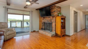 A living room with a fireplace, a ceiling fan, and a large window overlooking a deck. - Lakefront Oasis:Big Back Porch, Private Pool & Hot Tub! All on Lake Chickamauga  (Decatur)