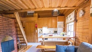 A cozy cabin interior with a wooden dining table, a sofa with cushions, a fireplace, and a kitchen area with a microwave and refrigerator. - Terwa-ukko 2 by Interhome (Hyrynsalmi)