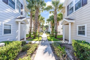 A residential street with two-story houses, a sidewalk, and palm trees. - Cozy 4BR Disney vacation Home 7-104 (Kissimmee)