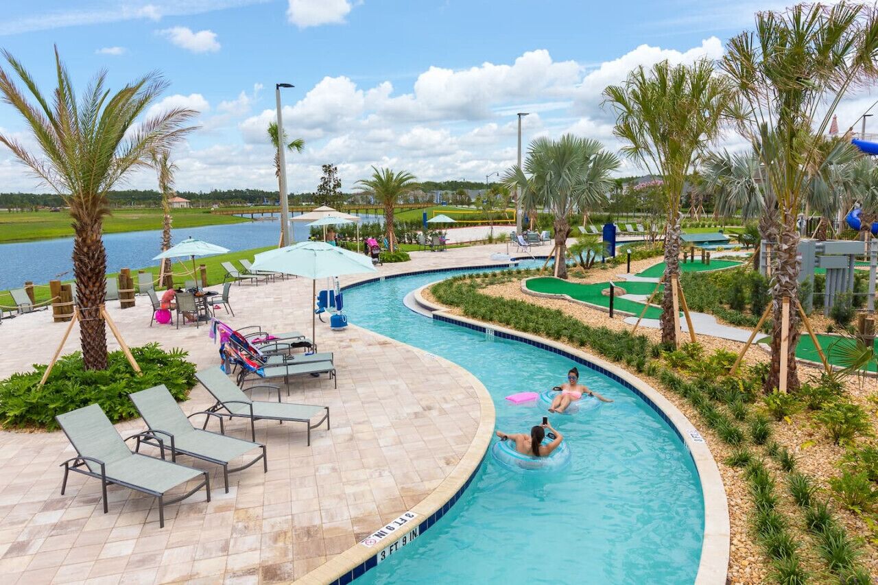 A pool area with lounge chairs, palm trees, and a view of a lake.