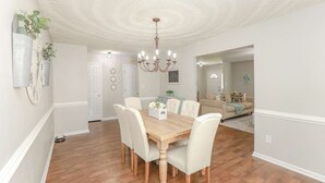 Un espace repas avec une table en bois, des chaises blanches et un lustre.