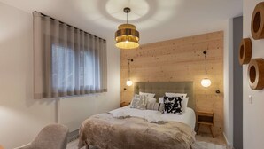A bedroom with a large bed, a chair, a wooden headboard, and a ceiling light fixture. - THELEME 102 (CHATEL)