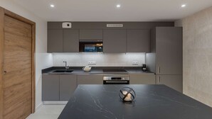 A modern kitchen with grey cabinets, a black marble countertop, and a wooden door. - THELEME 102 (CHATEL)