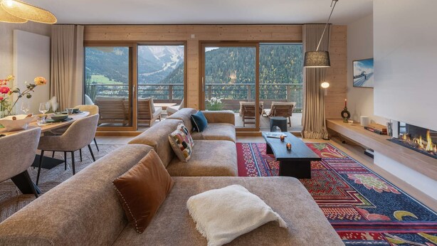 A modern living room with a large sofa, dining table, and chairs, a fireplace, and a view of mountains through large windows. - THELEME 102 (CHATEL)