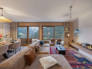 A modern living room with a large sofa, dining table, and chairs, a fireplace, and a view of mountains through large windows. - THELEME 102 (CHATEL)