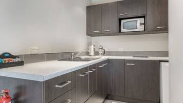 A modern kitchen with dark wood cabinets, a stainless steel sink, a microwave, and a kettle.