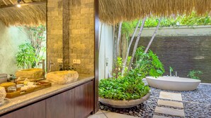 Une salle de bain avec un lavabo en pierre, un grand miroir et un toit de chaume.