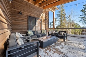 A wooden deck with outdoor seating, including a sofa and chairs, and a fire pit.