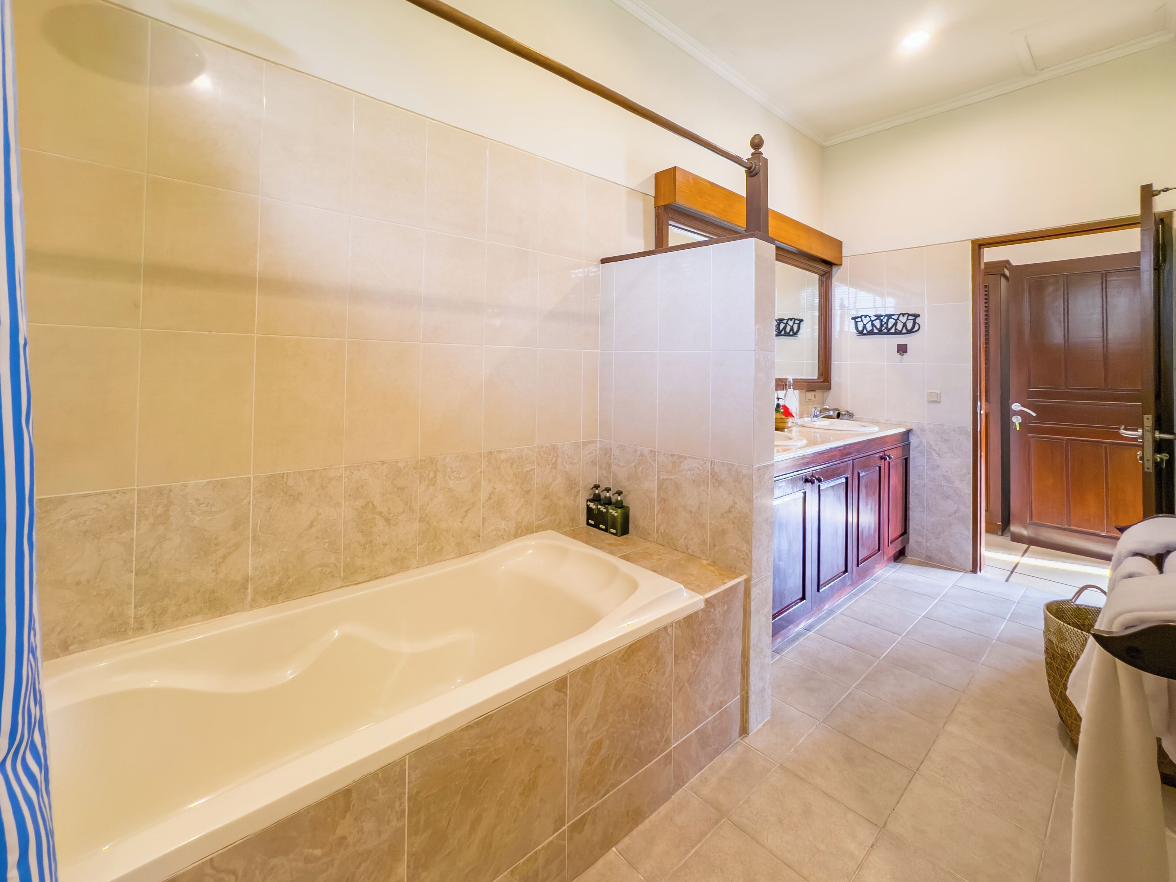 A modern bathroom with a large bathtub, a wooden vanity with a mirror, and a door leading to another room.