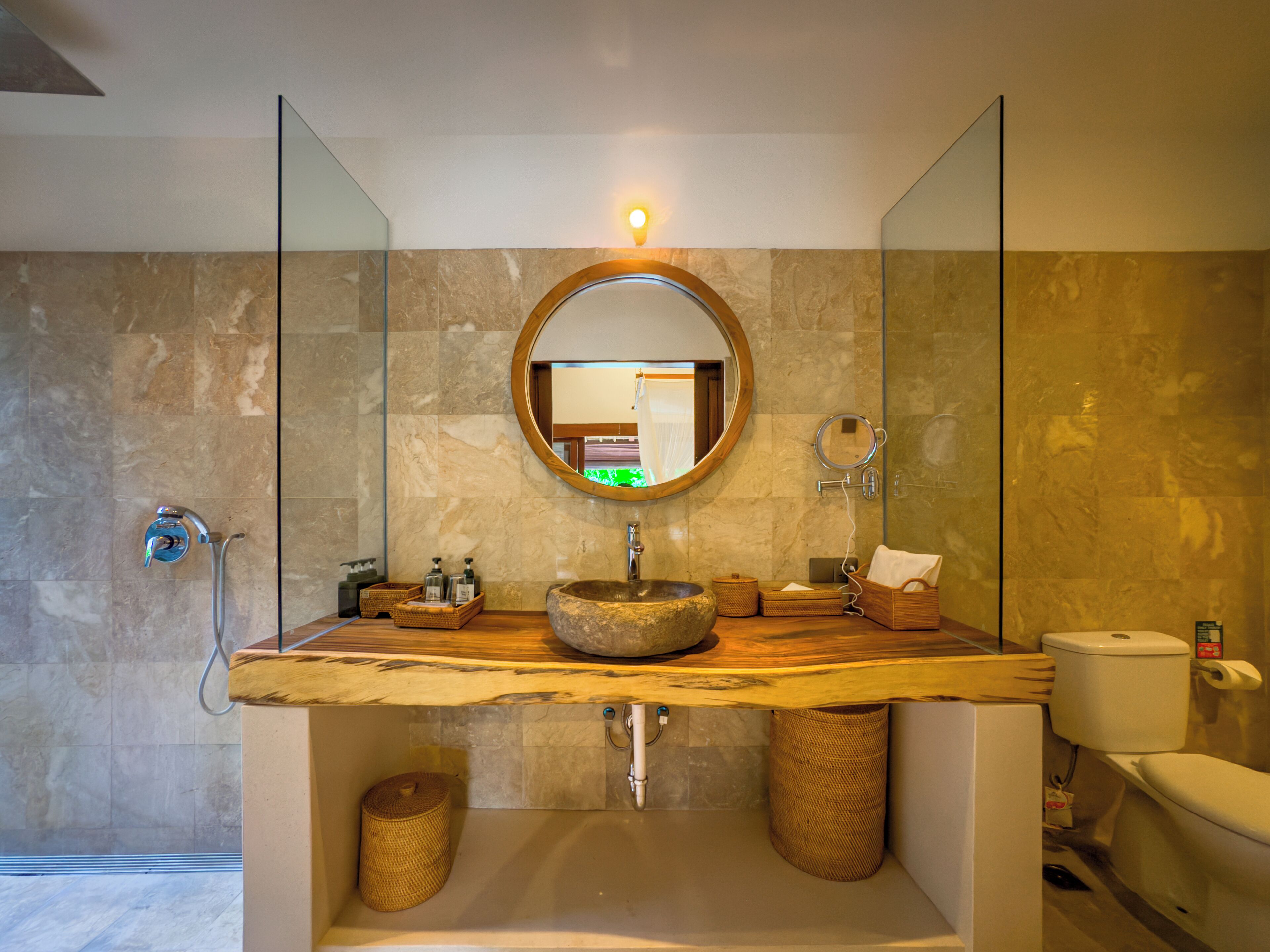 Une salle de bain moderne avec un lavabo en pierre, un miroir rond et des toilettes.
