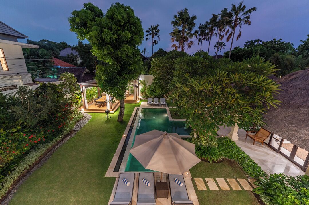 A swimming pool with lounge chairs, surrounded by lush greenery and palm trees.