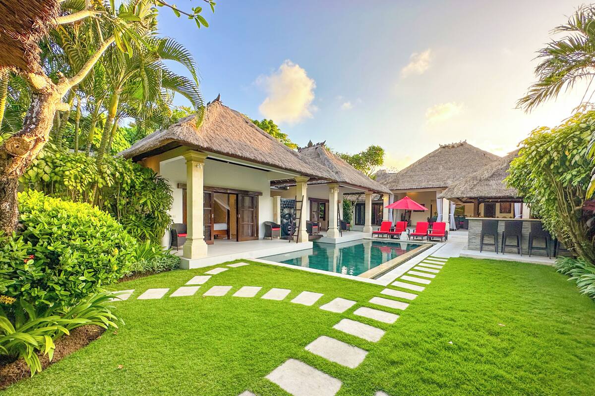 A resort with a swimming pool, thatched-roof structures, and a well-maintained lawn.