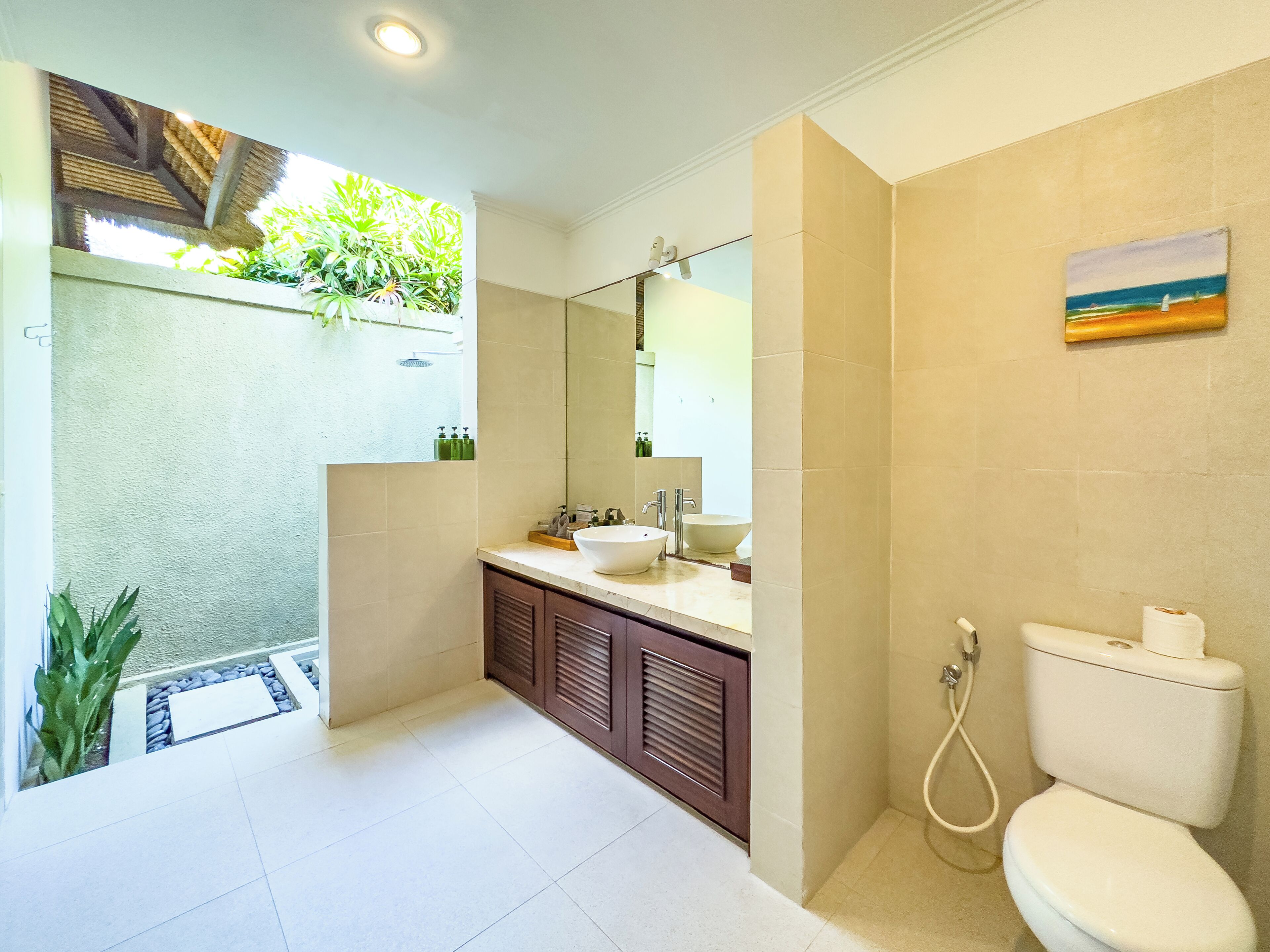 A modern bathroom with a large sink, mirror, and toilet. There is a shower area with a glass door and a small plant.