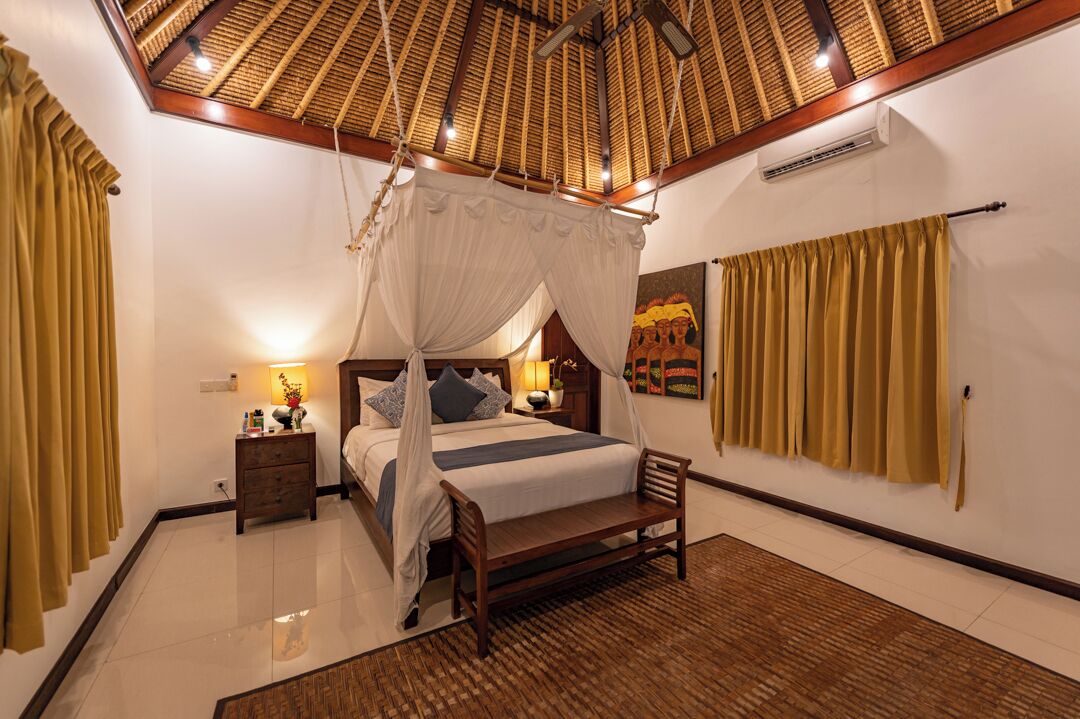A bedroom with a four-poster bed, a wooden bench, a nightstand, and a wall-mounted air conditioning unit.