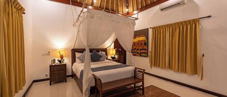A bedroom with a four-poster bed, a wooden bench, a nightstand, and a wall-mounted air conditioning unit.