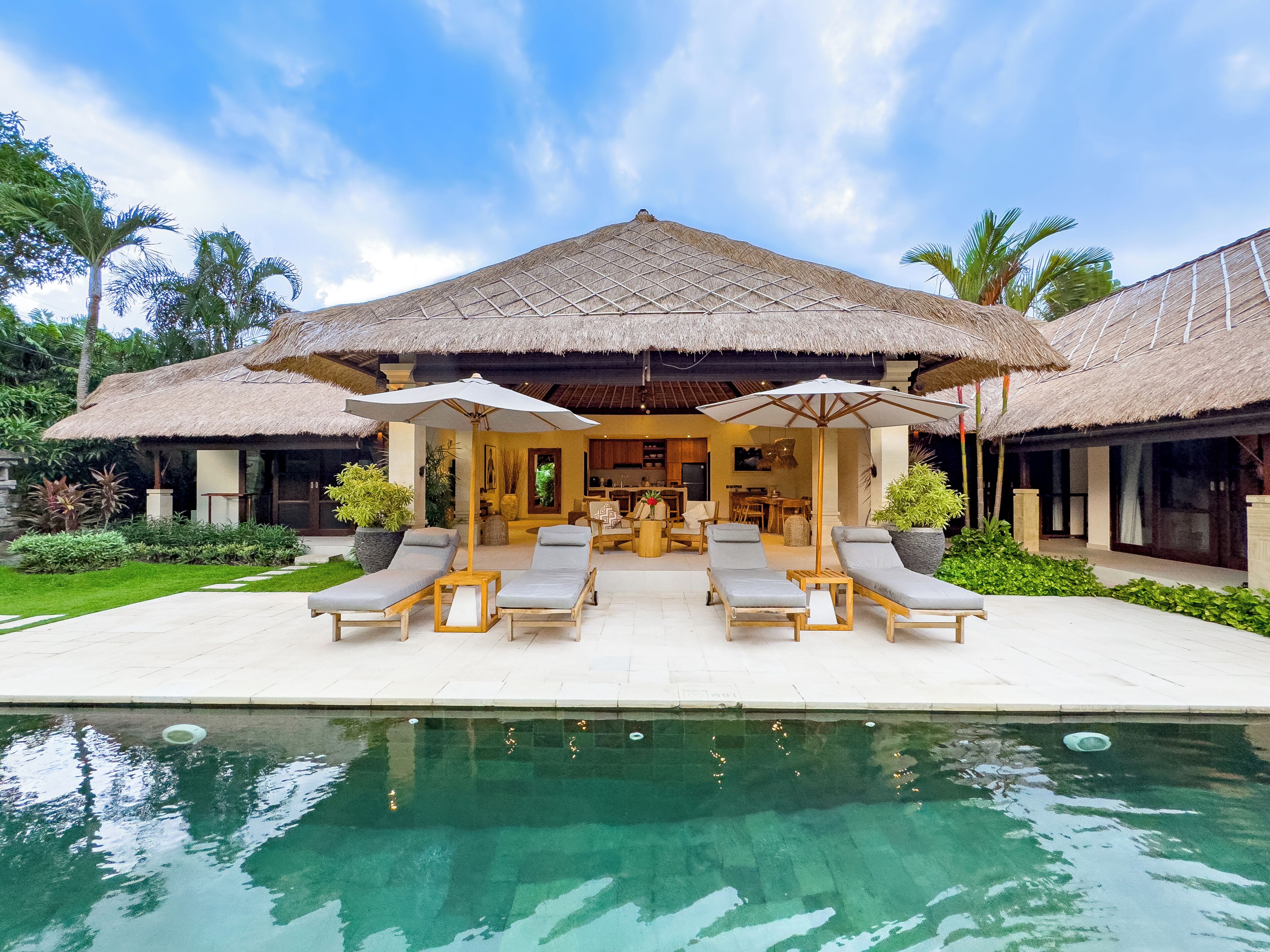 Un resort con piscina, sillones de descanso y una estructura de techo de paja.