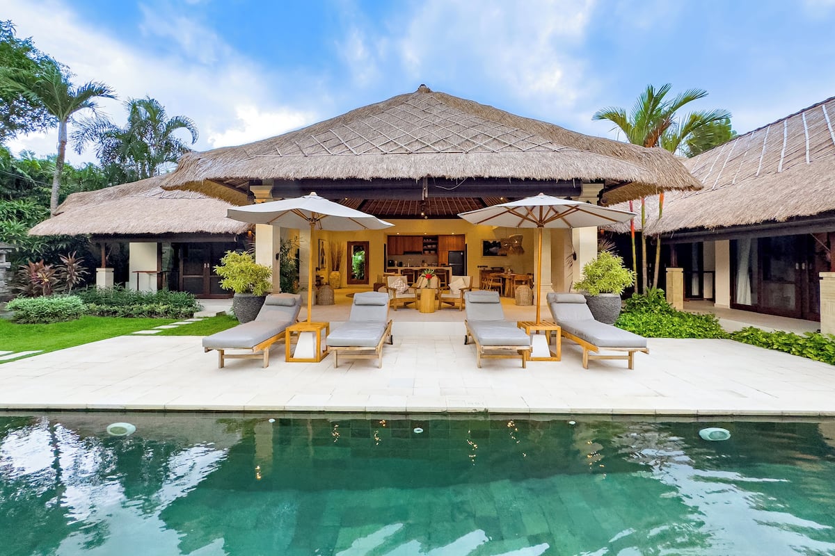 A resort with a pool, lounge chairs, and a thatched-roof structure.