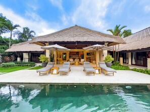 A resort with a pool, lounge chairs, and a thatched-roof structure. - Villa Bugis Seminyak (Seminyak)