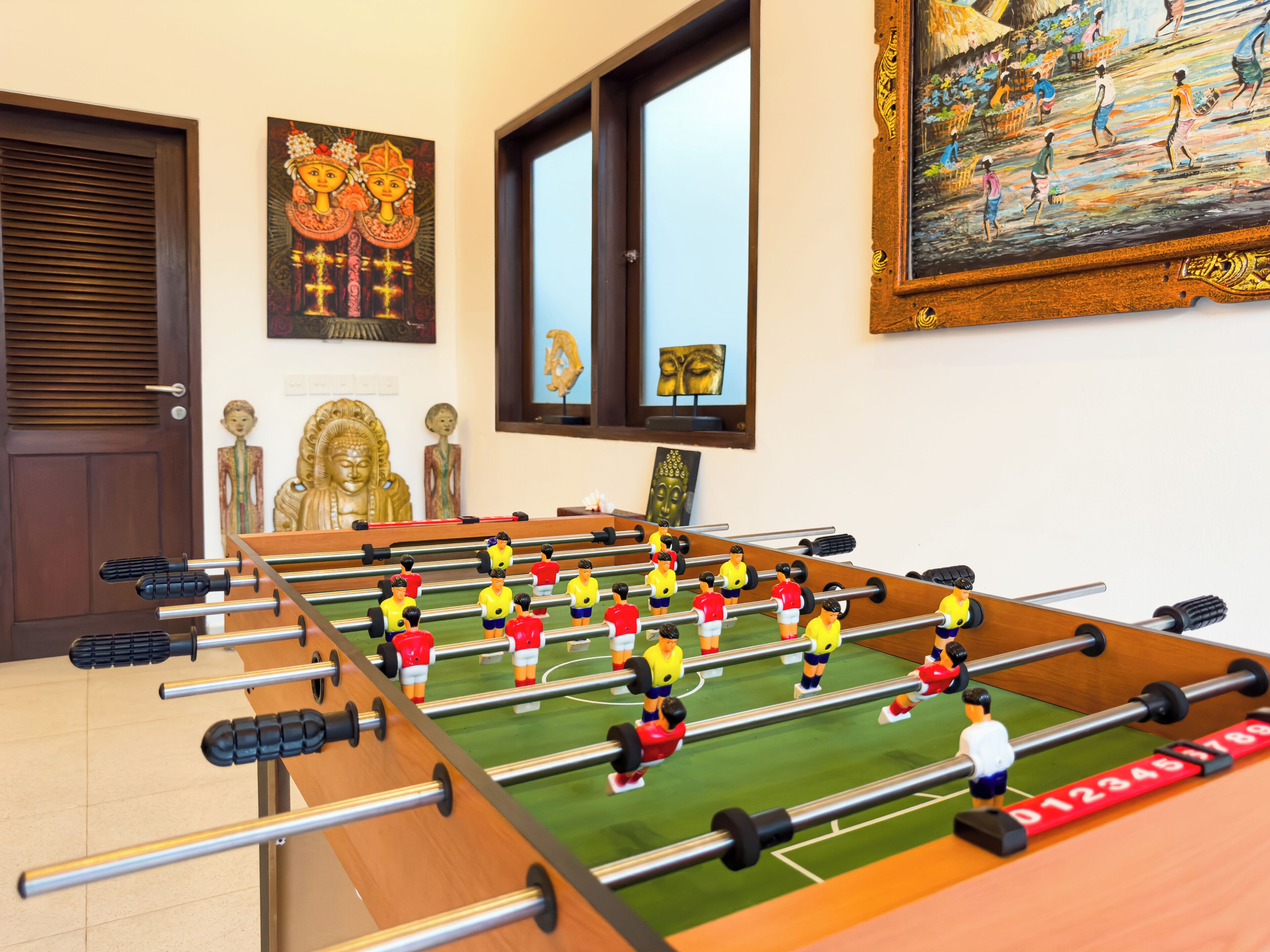 A foosball table in a room with a Buddha statue, a painting, and a window.