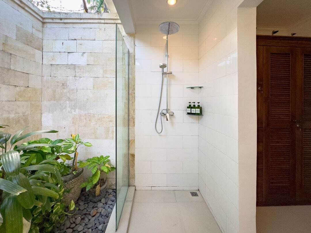 A small, tiled shower area with a handheld showerhead, a glass door, and a wooden door in the background.
