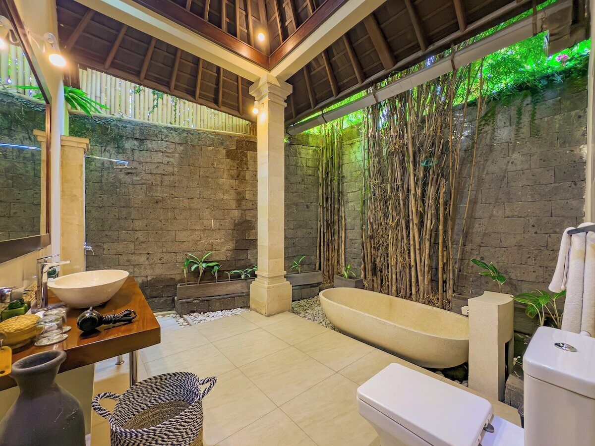 Une salle de bain avec une grande baignoire, un lavabo et des toilettes. On y trouve des plantes et un mur en bambou.