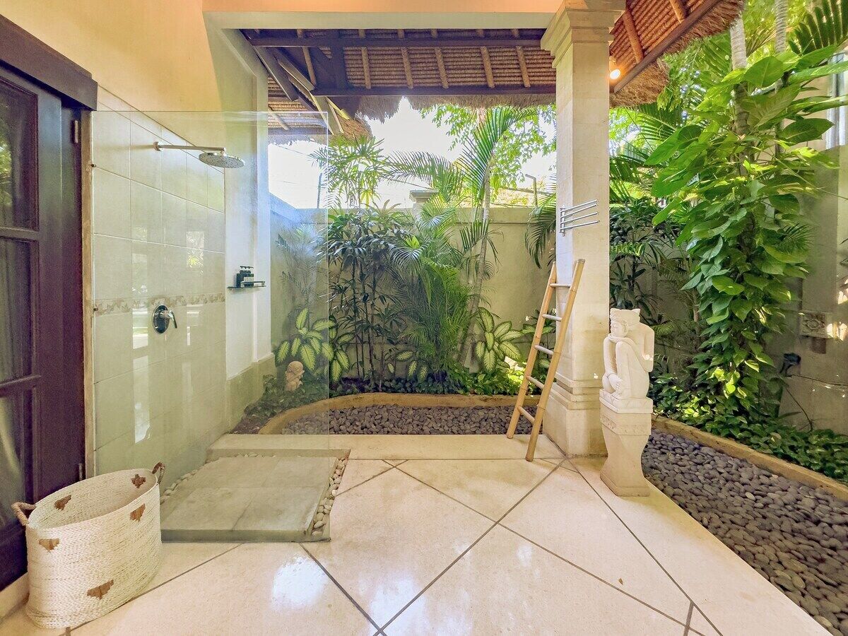 A modern bathroom with a glass-enclosed shower, a stone pathway, and lush tropical plants.