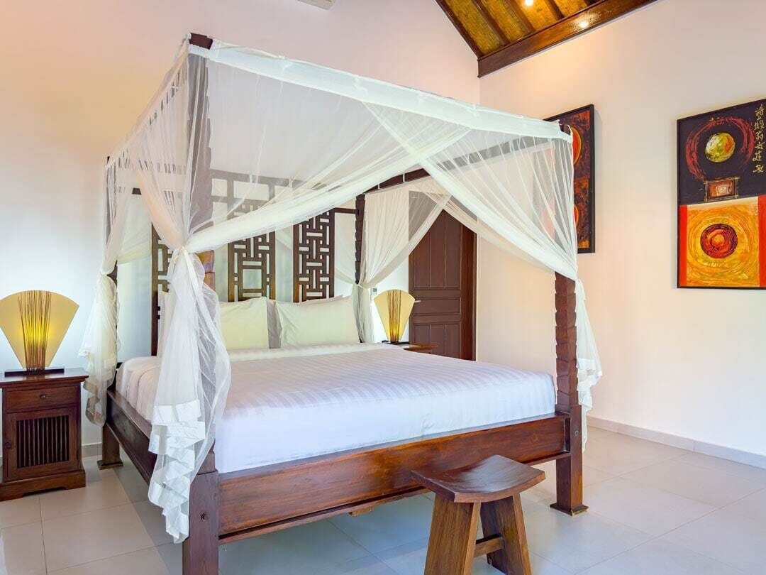 A four-poster bed with a canopy, wooden nightstands, a bedside table, and a wall-mounted lamp.