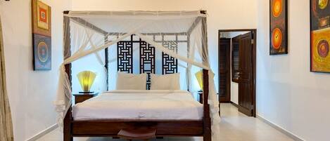A four-poster bed with a canopy, a bedside table with a lamp, and artwork on the walls.