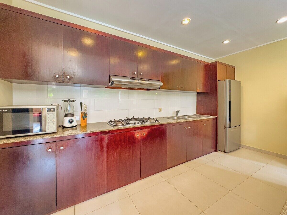 Una cocina con armarios de madera, microondas, licuadora, estufa a gas y refrigerador.